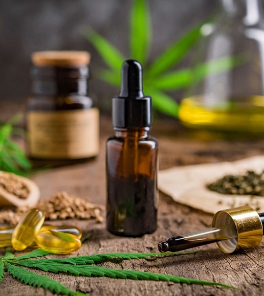 Huile de CBD en flacon compte-gouttes, capsules de chanvre, feuilles et graines sur table rustique.